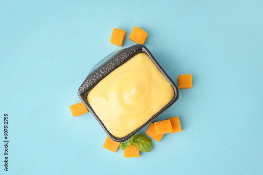 Bowl with tasty cheddar cheese sauce on blue background