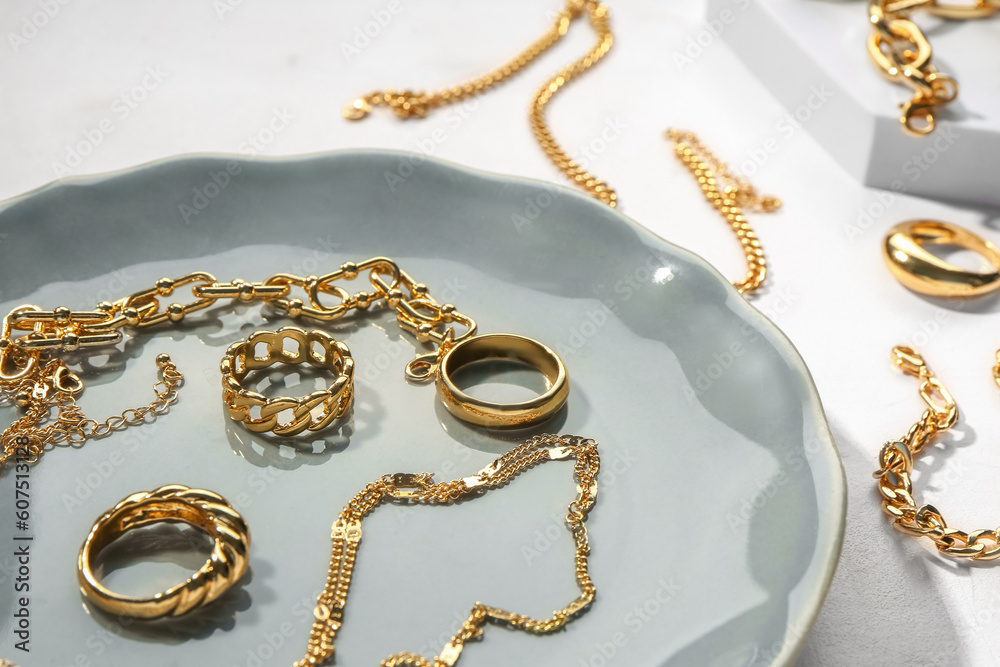 Plate and decorative podium with golden jewellery on white background