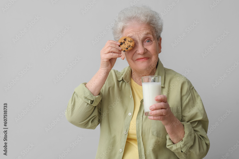 Senior woman with glass of milk and cookie on grey background