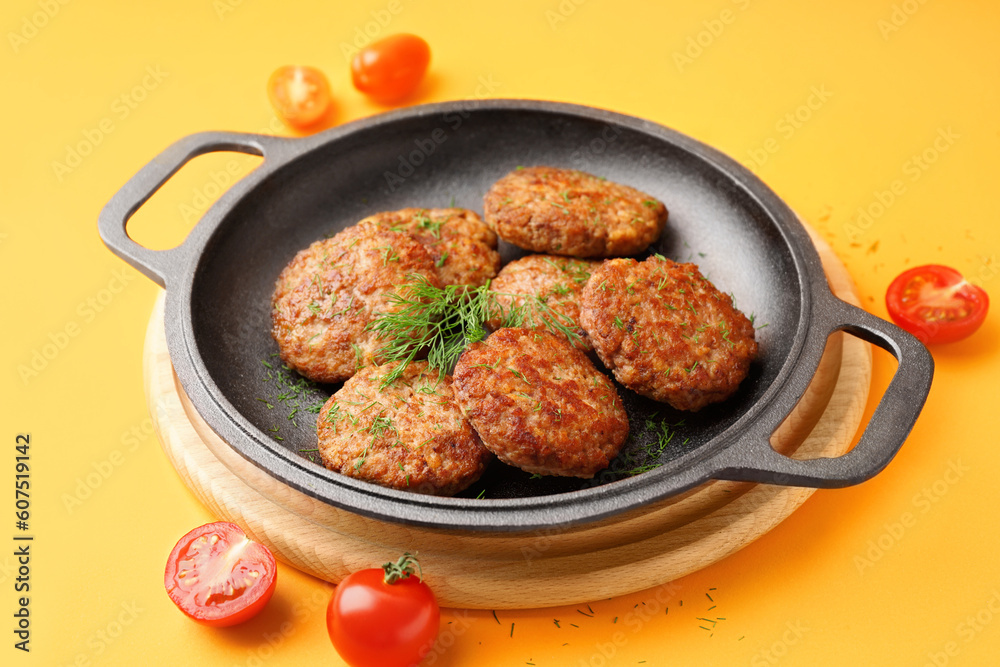 Frying pan with cutlets, dill and tomatoes on yellow background