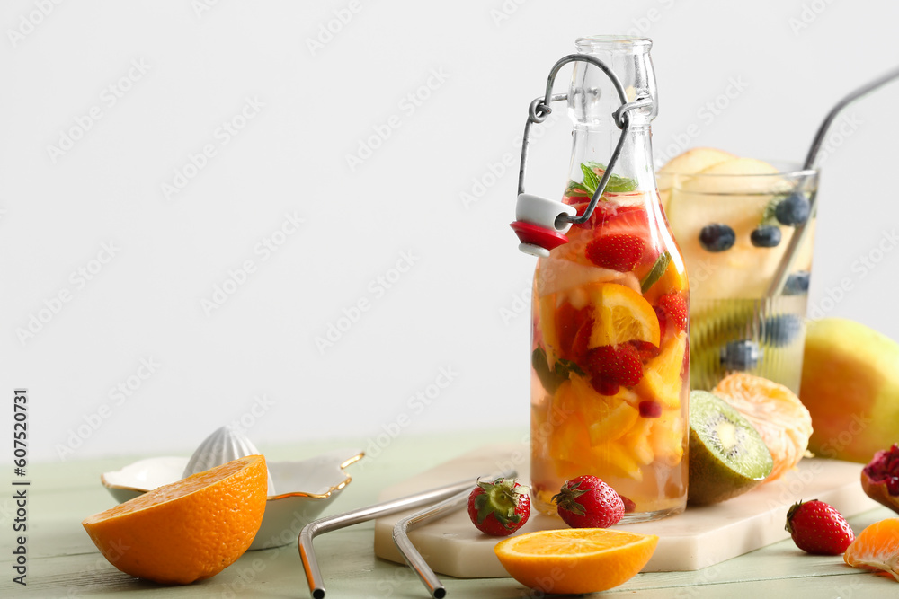 Glass and bottle of infused water with different sliced fruits on green wooden table