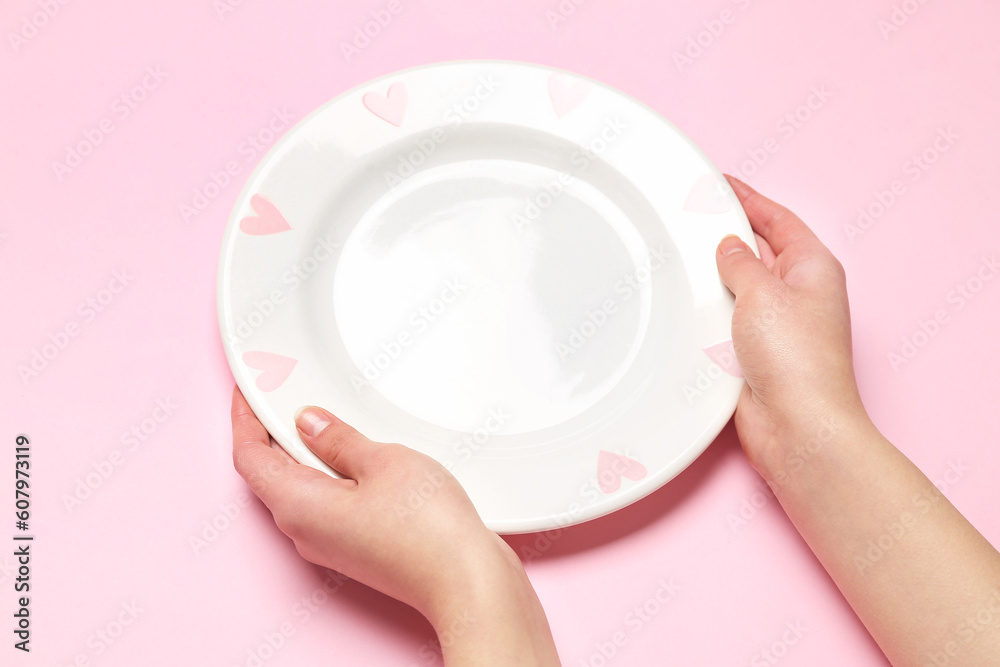 Female hands with empty plate on pink background