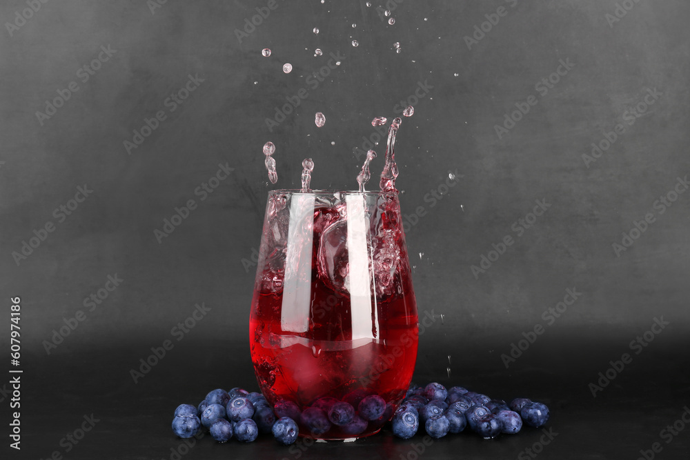 Glass of tasty blueberry cider with splashes, ice cube and berries on dark background