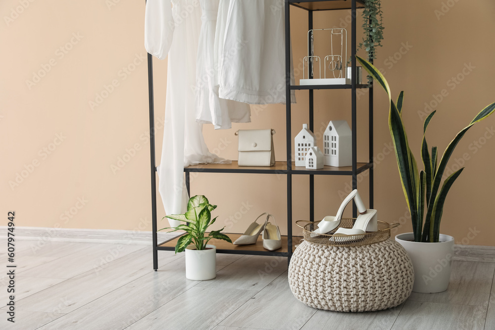 Shelving unit with clothes, accessories and houseplants near beige wall