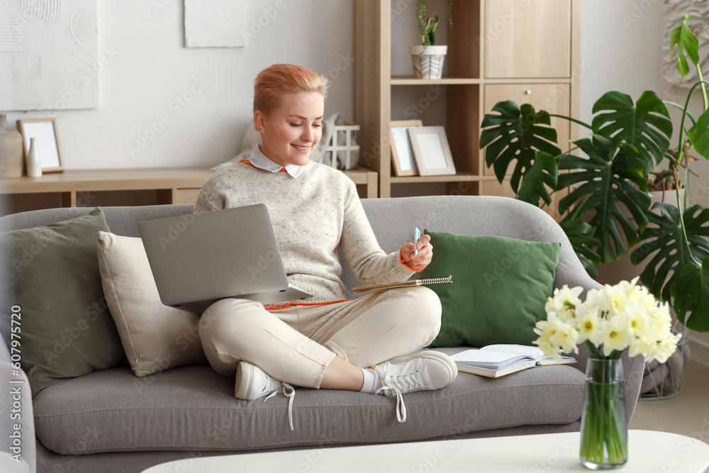 Female student studying with laptop on sofa at home