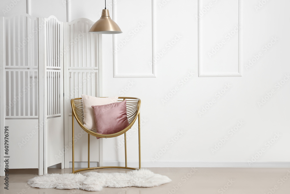 Cozy armchair with cushions and folding screen near white wall