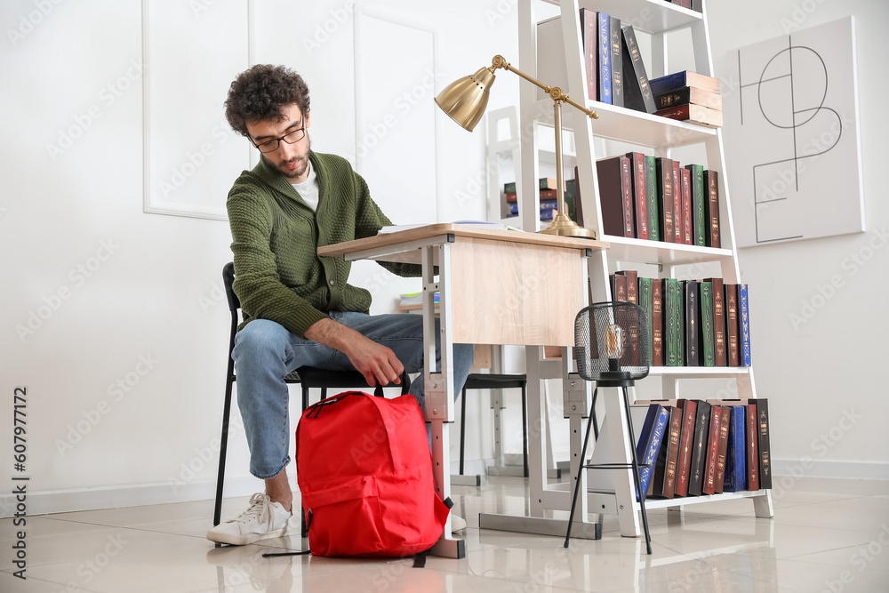 Male student with backpack sitting at table in library