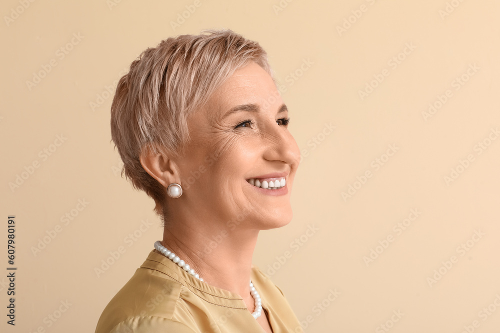 Mature woman with pearl jewelry on beige background, closeup