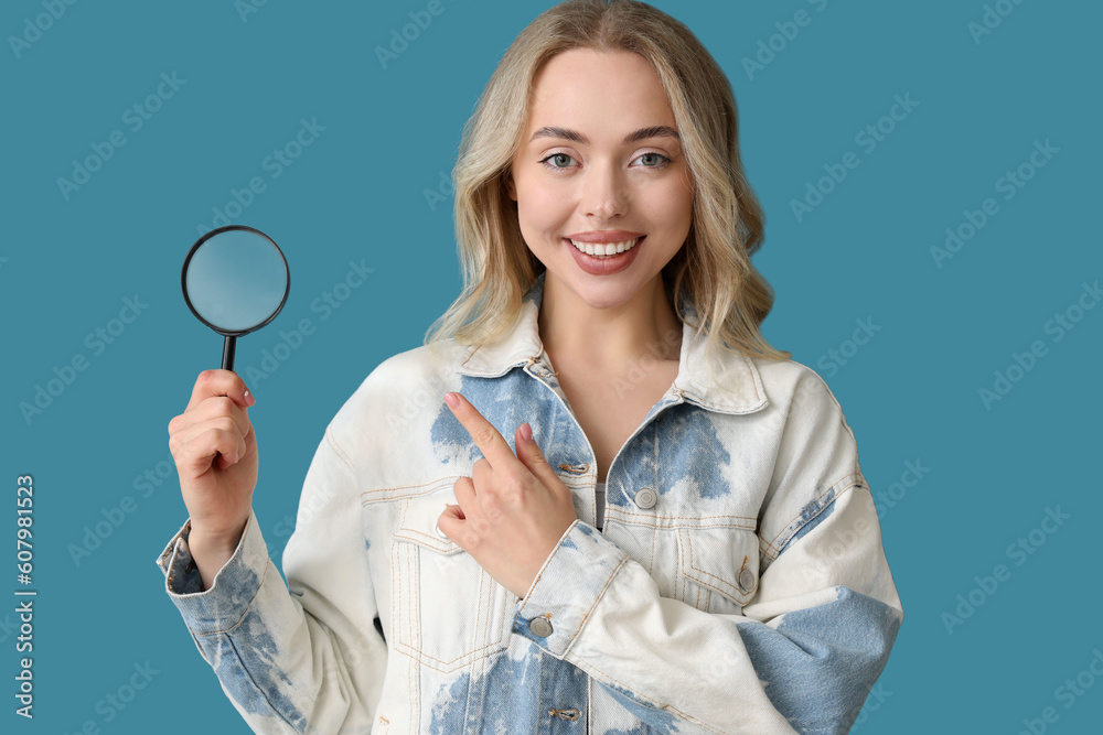 Young woman pointing at magnifier on blue background