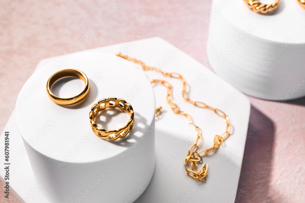 Decorative podiums with beautiful golden jewellery on pink textured background