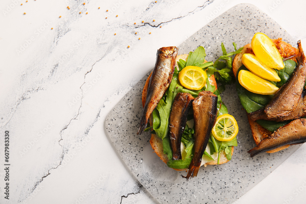 Board of tasty sandwiches with canned smoked sprats on white marble background