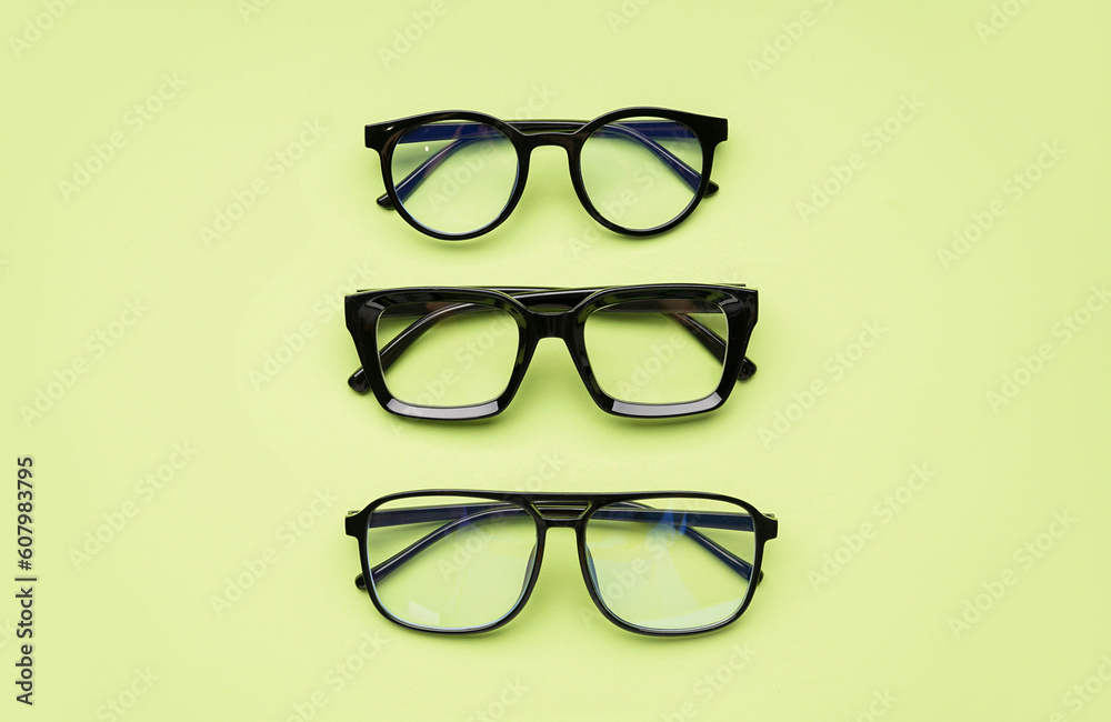 Stylish different black eyeglasses on green background