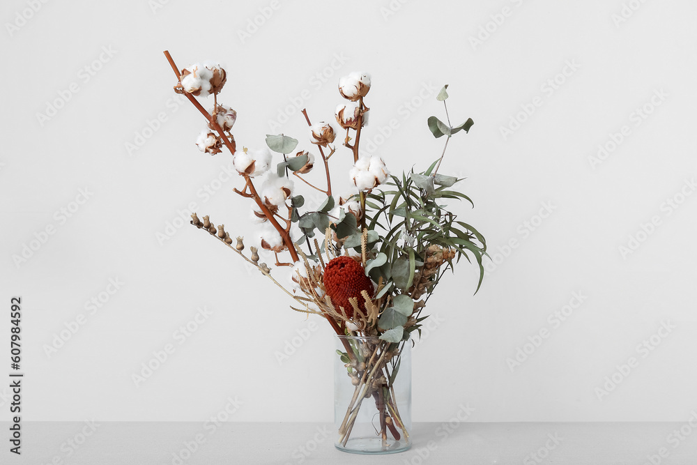 Vase of cotton sprigs, eucalyptus and plants on table near white wall