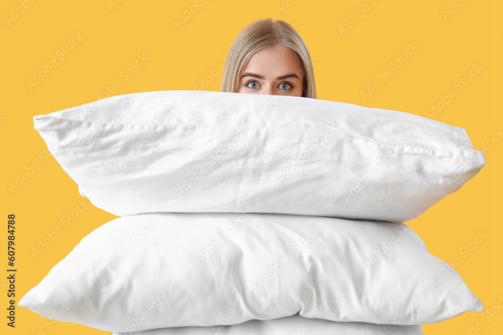 Young woman with pillows on yellow background