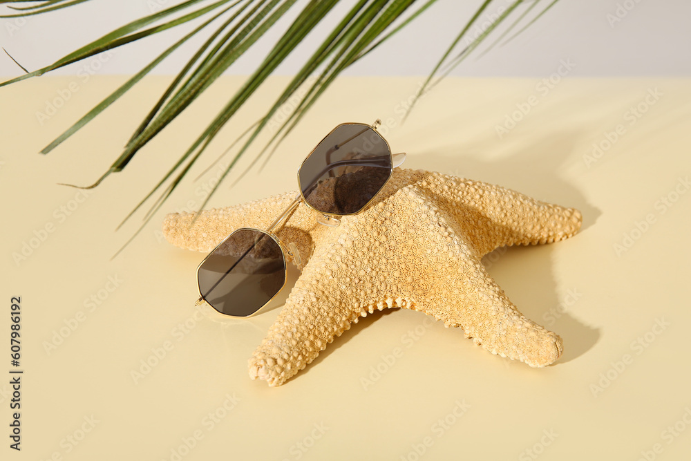 Stylish sunglasses with starfish and palm leaf on light table