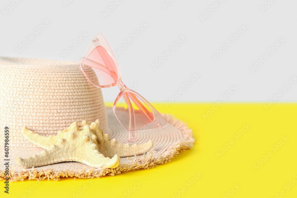 Stylish sunglasses and hat with starfish on yellow table