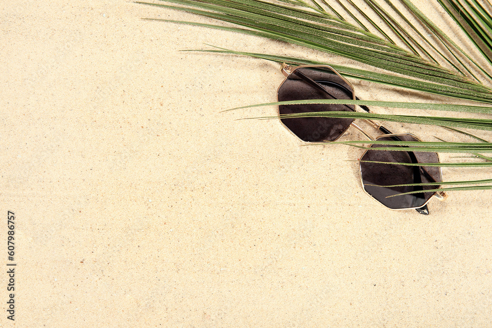 Palm leaf with stylish sunglasses on beige background