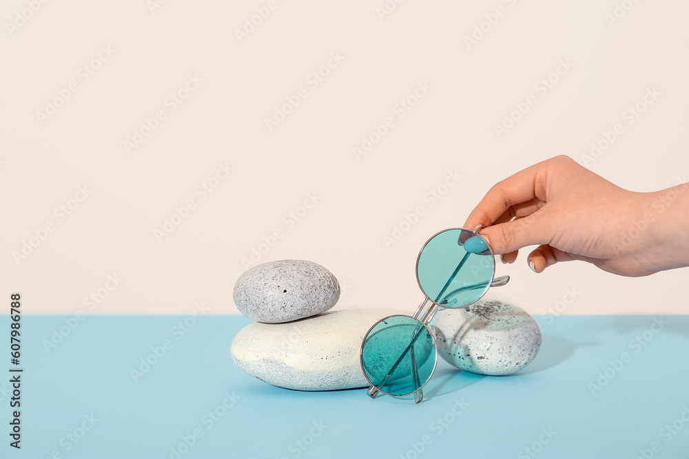 Female hand and stones with stylish sunglasses on blue table