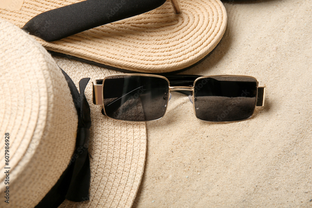 Stylish sunglasses with hat and flip flops on sand