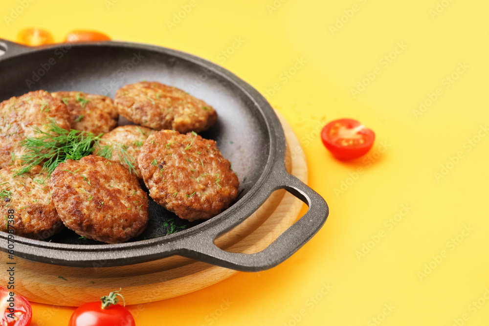 Frying pan with cutlets, dill and tomatoes on yellow background