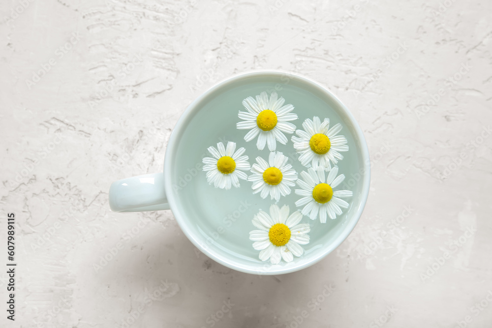 Cup with water and chamomile flowers on light background