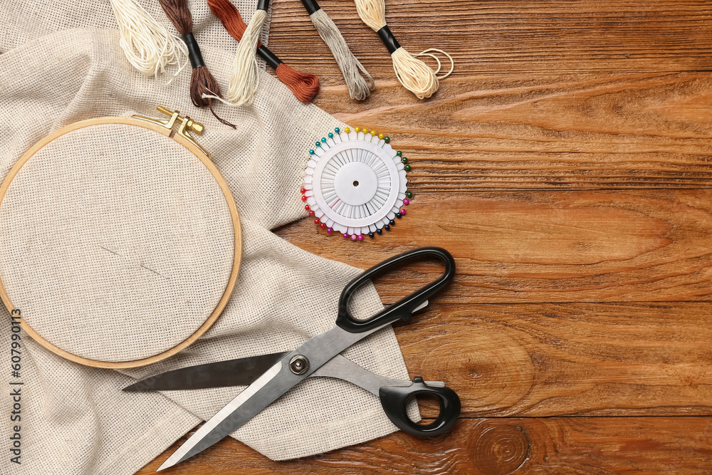 Embroidery hoop with canvas, mouline threads and scissors on brown wooden background