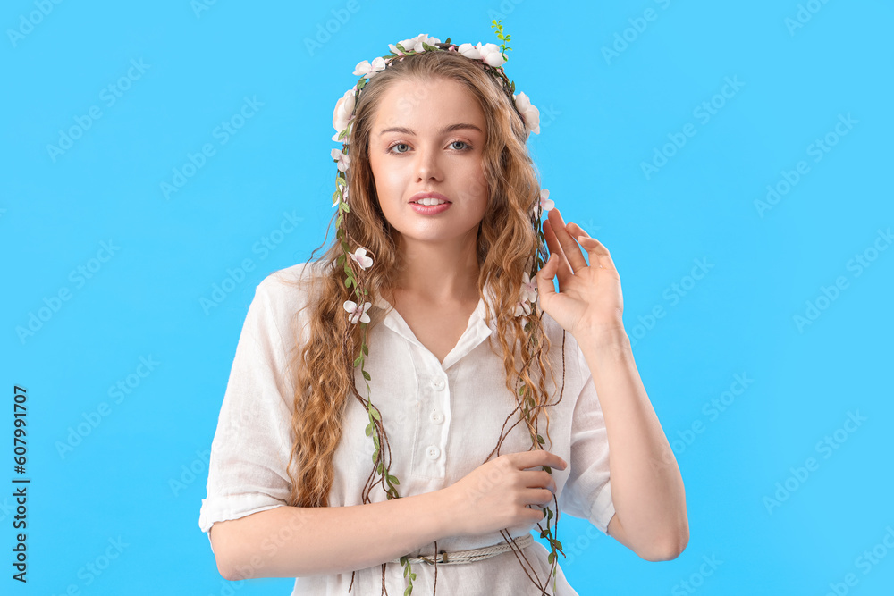 Beautiful young woman with flowers in her hair on blue background. Summer solstice