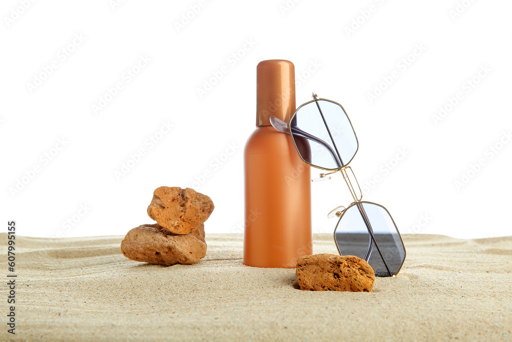 Bottle of sunscreen cream with stones and sunglasses at sand isolated on white background