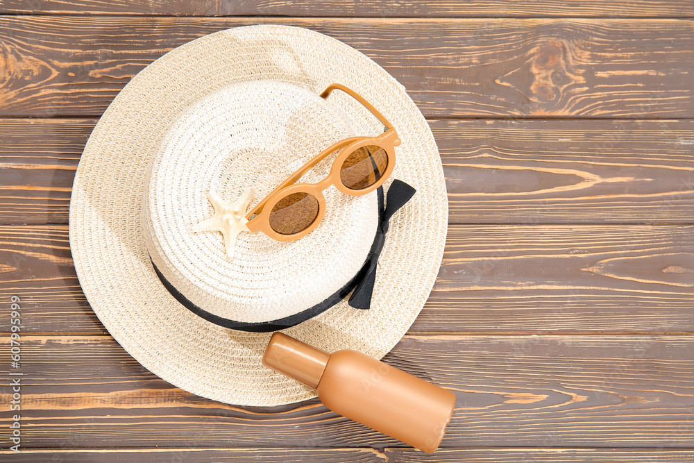 Bottle of sunscreen cream, sunglasses and wicker hat on wooden background