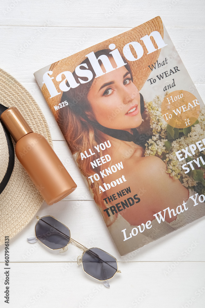 Bottle of sunscreen cream, sunglasses, magazine and wicker hat on light wooden background