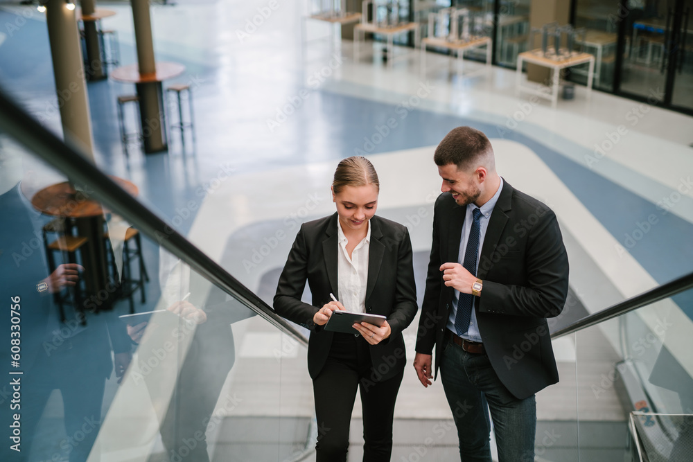 Two businesspeople using a digital tablet while going up the escalator..