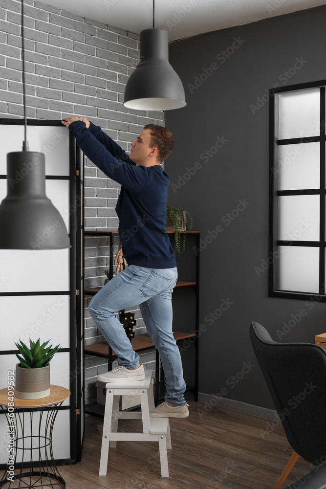 Young man on stepladder near folding screen in room