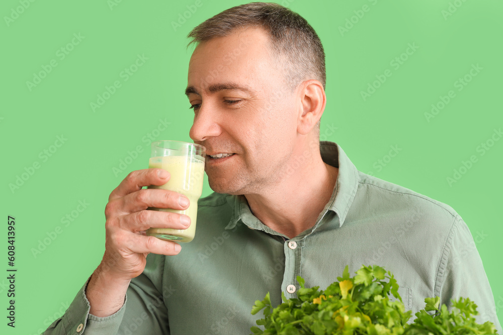 Mature man with glass of vegetable smoothie and parsley on green background, closeup