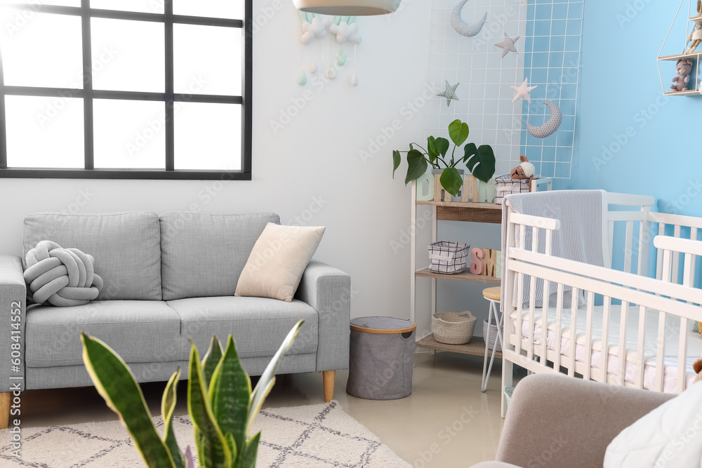 Interior of stylish bedroom with baby crib, sofa and shelving unit