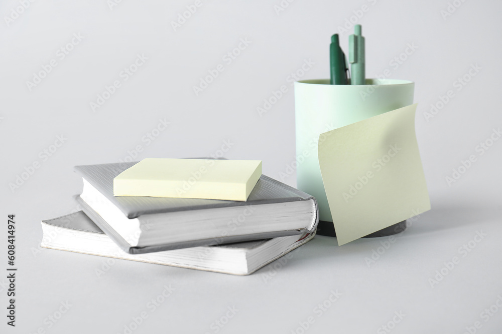 Pen holder with sticky notes and books on grey background