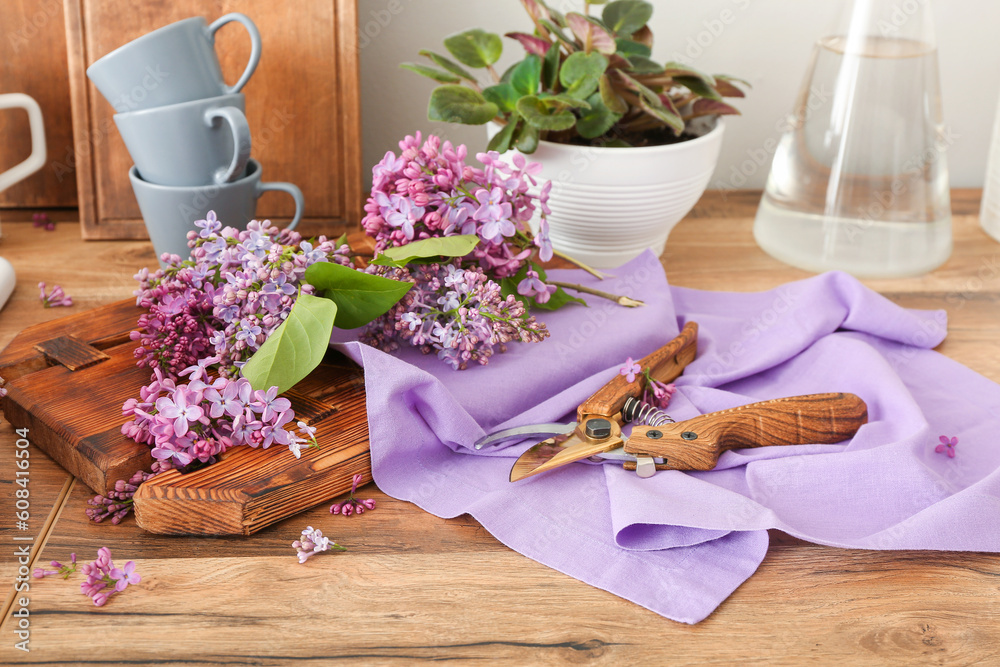 Garden shears and lilac twigs on wooden table