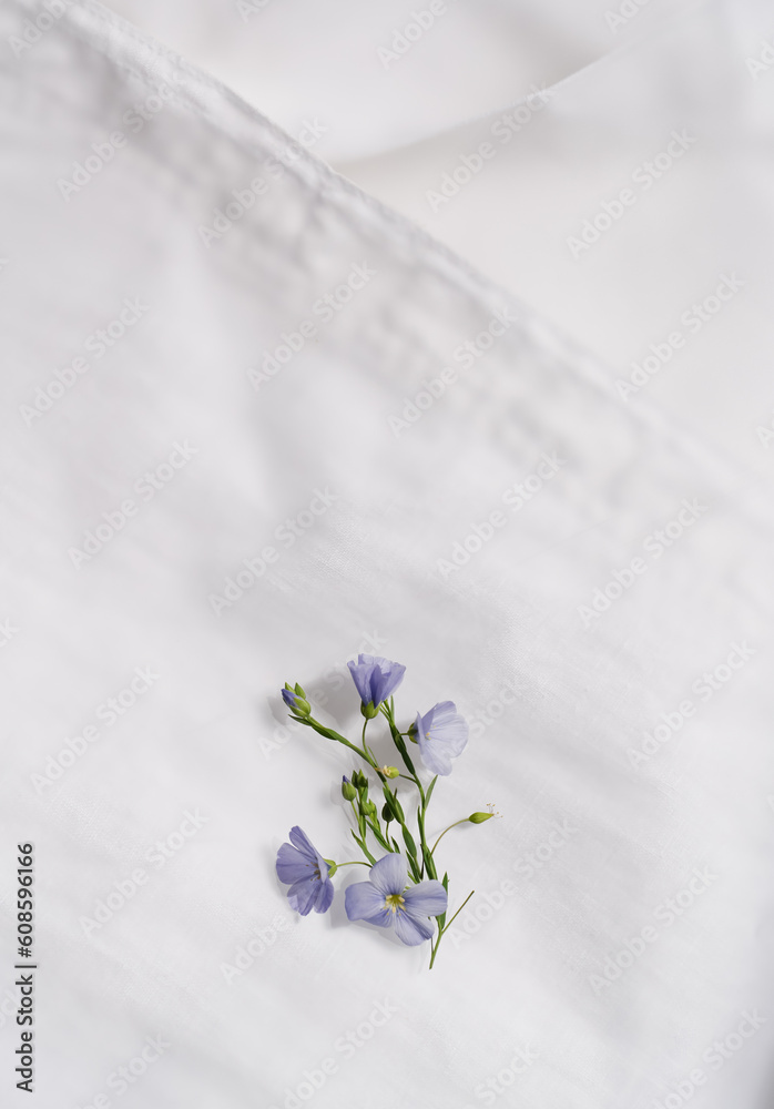 Beautiful fresh tiny flowers of flax on blurred textured white linen clothes