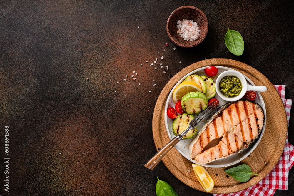 Grilled salmon steaks with spices, lemons and grilled zucchini on wooden board. Top view of fried fi