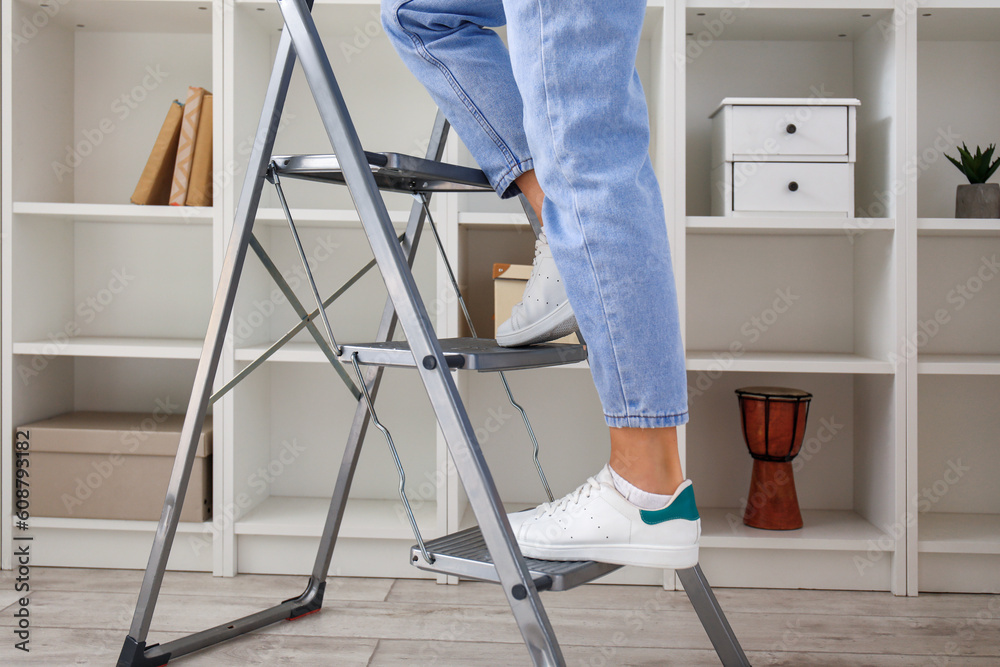 Young woman on stepladder near bookshelf at home, closeup