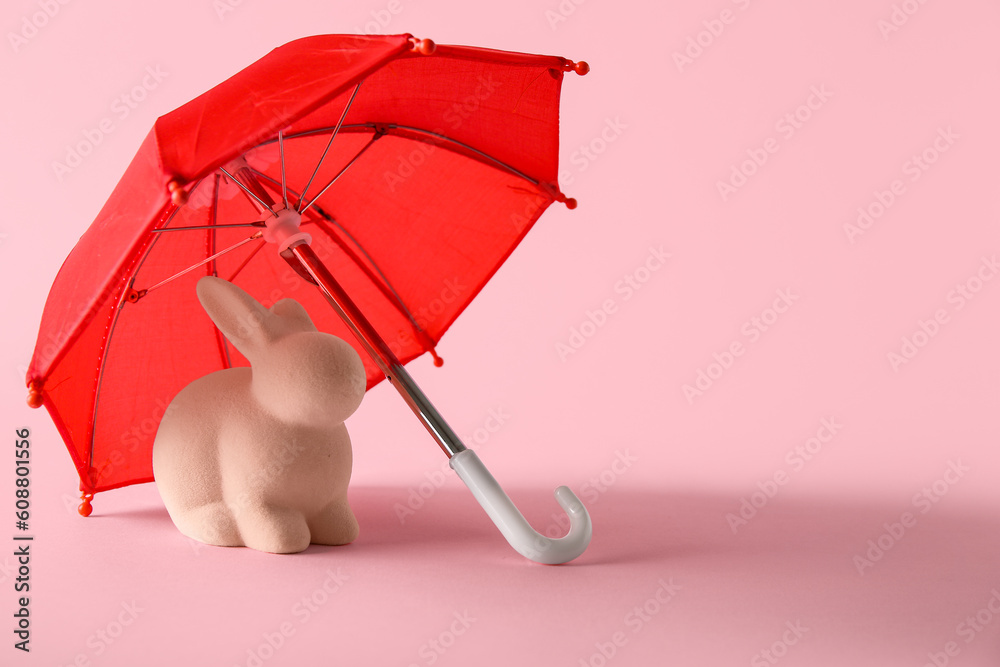 Creative composition with rabbit toy and red mini umbrella on pink background