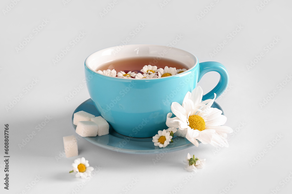 Cup of natural chamomile tea and flowers on white table near blue wall