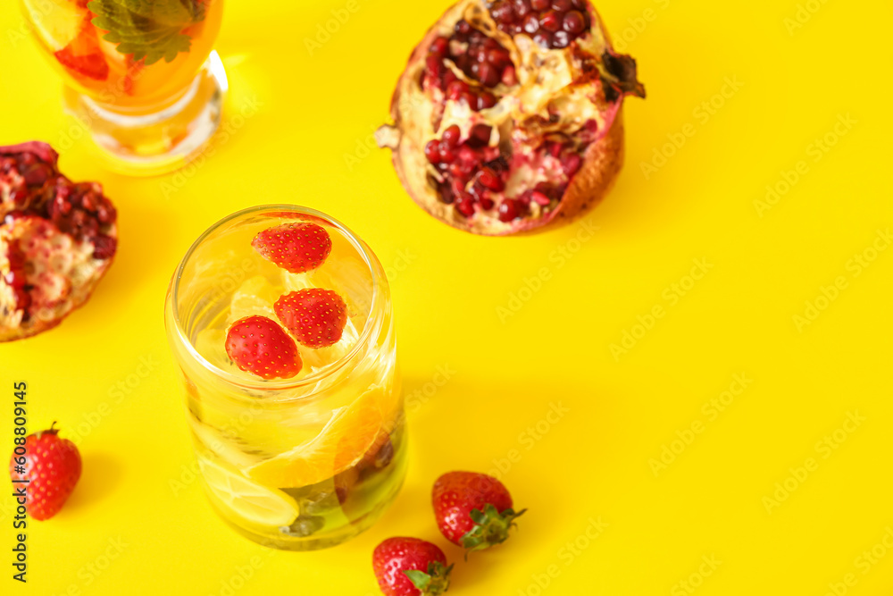 Glasses of infused water with different sliced fruits on yellow background