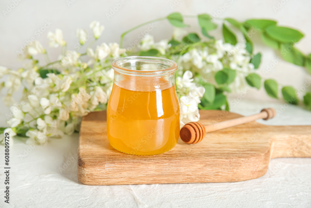 Jar of honey with flowers of acacia and dipper on light background, closeup