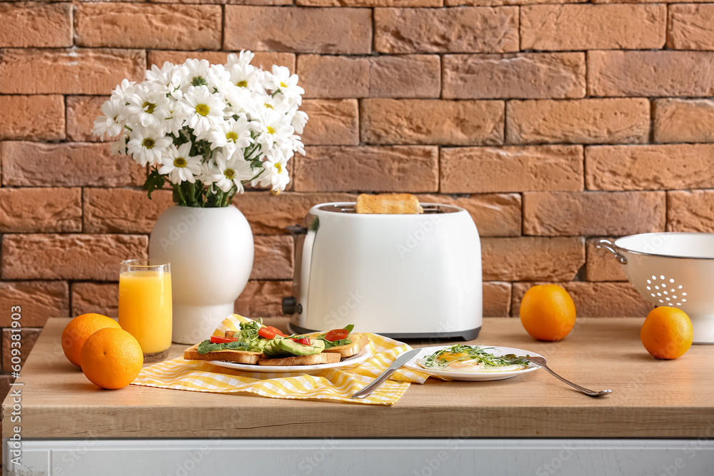 Modern toaster with crispy bread slices, toasts, fried eggs and glass of orange juice on table