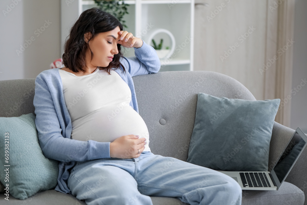 Tired young pregnant woman working with laptop at home