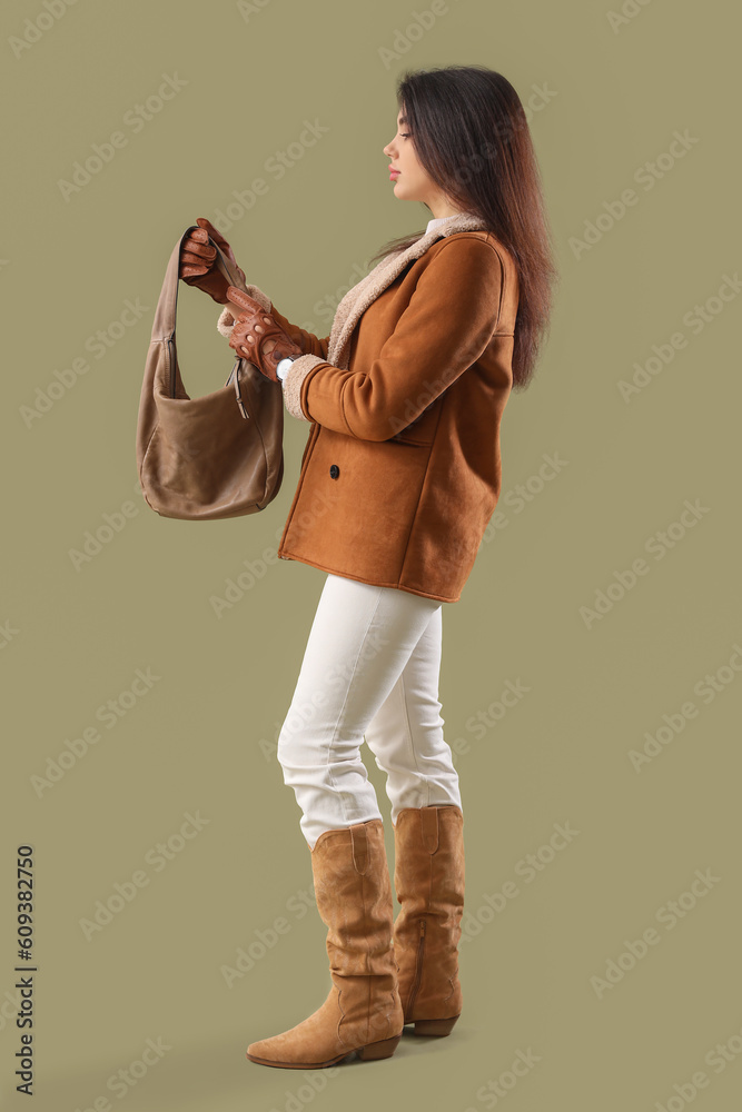 Stylish young woman in leather gloves with bag on green background