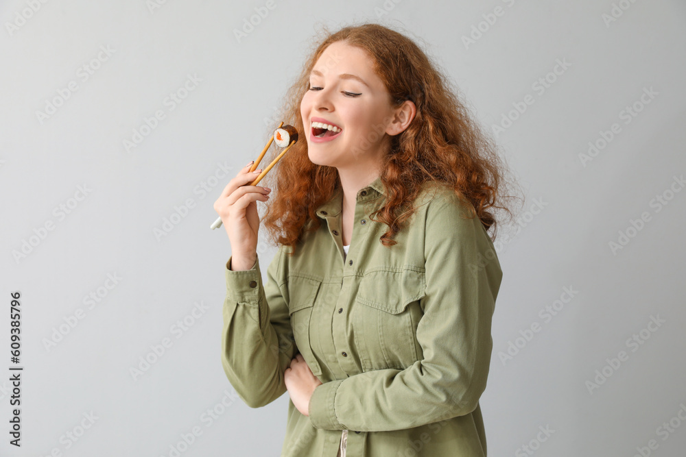 Young woman with sushi roll on light background