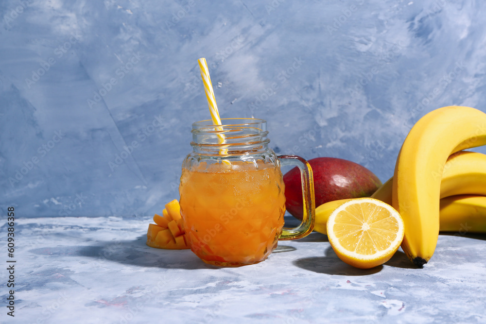 Mason jar of fresh mango smoothie and fruits on blue background