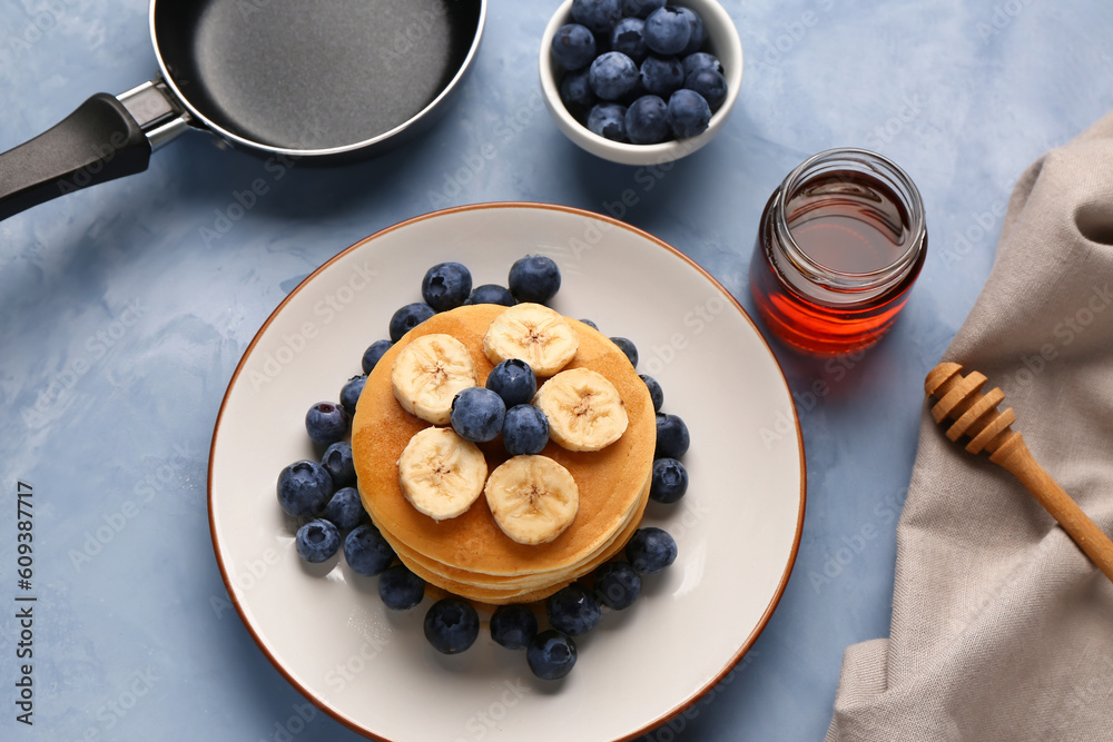 Plate with sweet pancakes, honey and frying pan on blue background