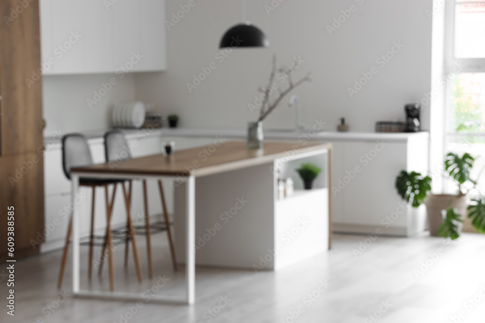 Interior of modern kitchen with island, chairs and white counters, blurred view